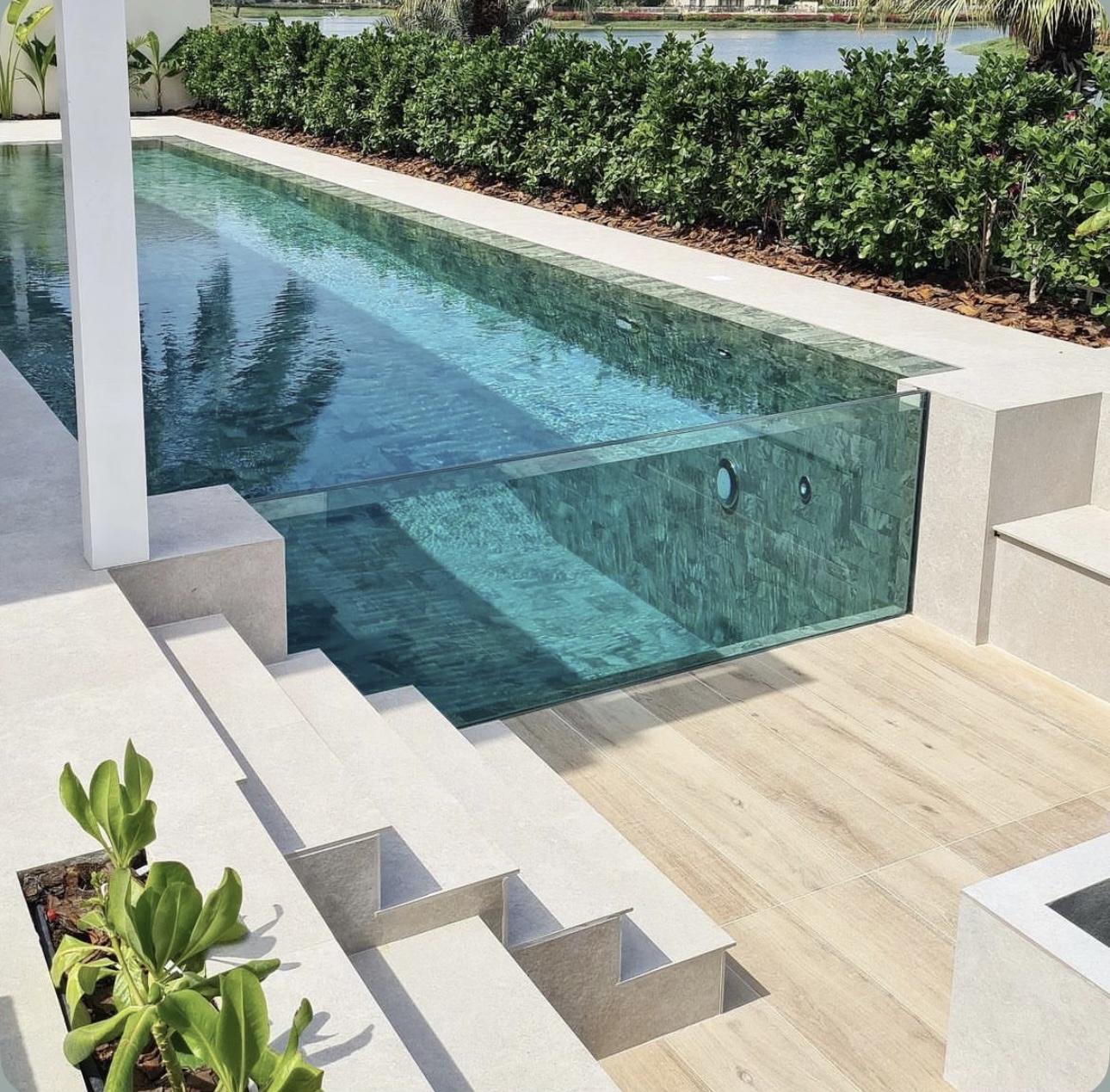 Luxury pool with a transparent glass wall, wide entry steps and green tiled interior